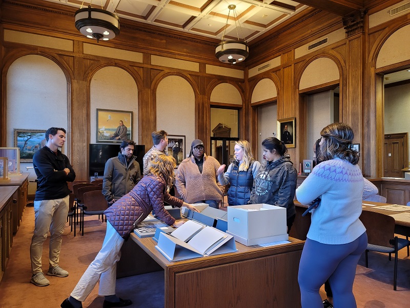 A small group of undergraduate students gather around archival items in a special collections reading room.